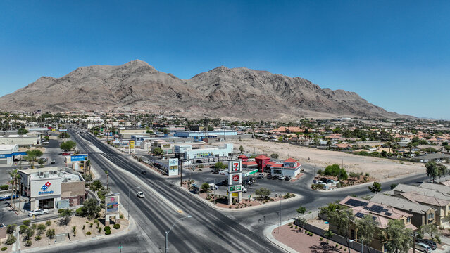 Aerial view of a desert city's landscape, where a long road stretches toward the base of majestic mountains, Las Vegas, Nevada, United States.