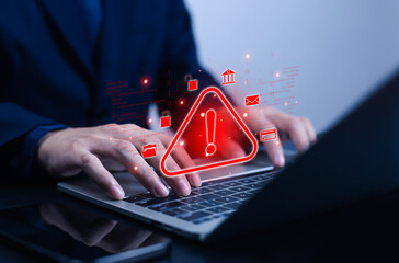 Hands typing on laptop with glowing red warning alert symbol, representing cybersecurity risk, online data breach, hacking attack, phishing scam, malware, fraud, and digital information security.