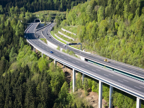 Aerial view of a ribbon of highway cutting through the verdant forest, with vehicles winding towards a dark tunnel, Lavanttal, Wolfsberg, Carinthia, Austria.