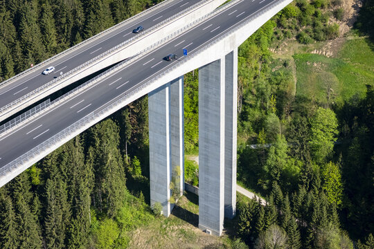 Aerial view of a concrete highway bridge soaring over a dense forest, its grey pillars contrasting with the vibrant green canopy, Wolfsberg, Carinthia, Austria.