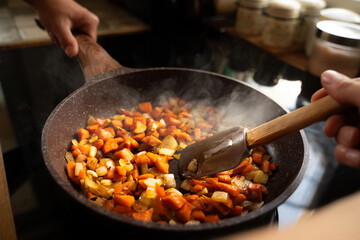 Close-up of woman's hands frying grated onions and carrots in a hot frying pan with vegetable oil on the induction stove, homemade cooking concept
