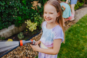 Smiling child watering garden with family during summer outdoors