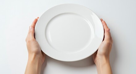 Two hands hold a white round empty ceramic plate on a white surface topdown view