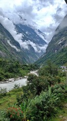 A scenic view of lush valley with a winding river, framed by towering mountains shrouded in mist and clouds under an overcast sky