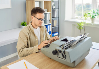 Writer typing on vintage typewriter in office. A focused man uses retro tools in a modern...