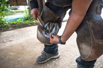 Close up unknown farrier nailing horseshoe in stable