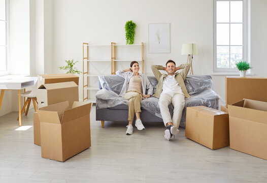 Smiling couple relaxing on sofa, moving boxes. In an apartment they pause during relocation and unpacking. Light fills the room as they enjoy a new home. Concept new home, fresh start.
