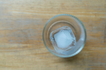 Top view of one square ice cubes in empty glass on wood background