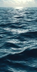 Fototapeta premium A vast expanse of deep blue ocean water ripples under the bright sunlight. The sun's reflection glimmers like a shimmering path across the sea