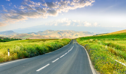 beautiful landscape of long road to amazing mountain scene from a green summer fields and hills. Asphalt road to mountains and golden meadows.