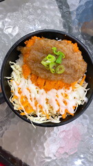 Japanese rice bowl with crispy chicken katsu, shredded cabbage salad, mayonnaise drizzle, savory sauce topping, and fresh green onion garnish, authentic Asian donburi meal served in black bowl