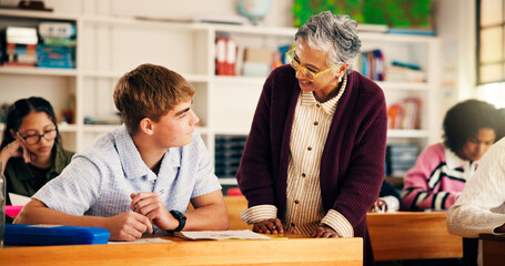 Teacher, teen boy and talk in classroom for test, advice or tips for development at high school. Mature woman, pupil and smile for discussion, inspection or learning support for education at academy