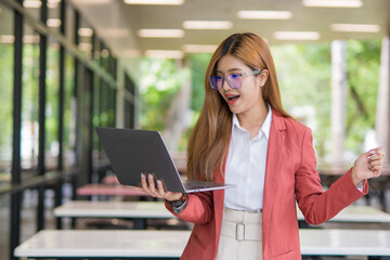 Fototapeta premium Asian businesswoman using digital laptop while standing in front of modern building. Attractive female employee working in front of office.