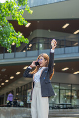 Fototapeta premium Asian businesswoman in suit using mobile phone while standing in front of modern business building.