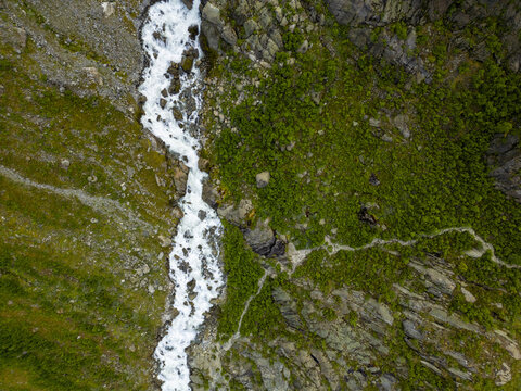 Aerial view of a raging river cutting through verdant slopes, showcasing nature's raw power and serene beauty, Buarbreen, Odda, Norway.