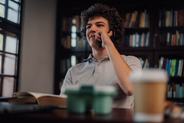 Student talking on phone while studying in library with books and coffee