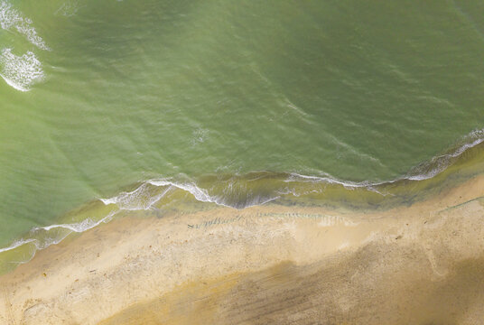 Aerial view of the sandy shore kissed by gentle waves, with the water's hues shifting from deep greens to light turquoise, Atlantico, Colombia.