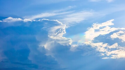 Beautiful and dramatic blue sky with large, puffy white clouds and a hint of a sunlit rainbow. An ideal background for themes of hope, nature, and meteorological concepts.