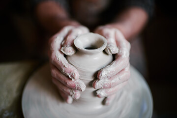 Caucasian middle aged man shaping clay on pottery wheel, hands covered in wet clay, focusing on creating ceramic vase, close up of skilled craftsmanship in pottery making process