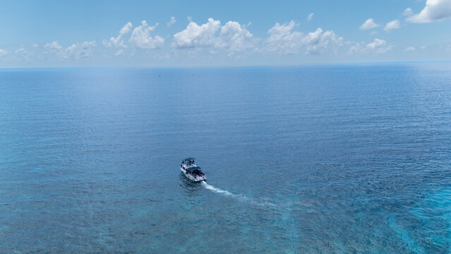Aerial view of a boat sailing through the turquoise waters, leaving a trail of white foam, under a sky dotted with fluffy clouds, San Andr&Atilde;&copy;s, San Andres and Providencia, Colombia.