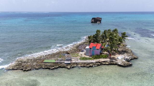 Aerial view of a vibrant, pastel-colored house nestled among swaying palms on a rocky islet, contrasted against the turquoise sea, San Andr&Atilde;&copy;s, San Andres and Providencia, Colombia.