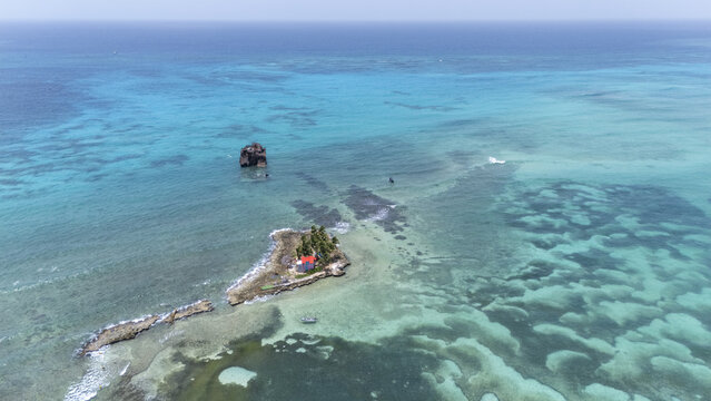 Aerial view of a tiny island with a red-roofed structure surrounded by shallow turquoise waters and distant dark rocks, San Andr&Atilde;&copy;s, San Andres and Providencia, Colombia.