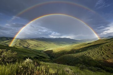 Obraz premium A stunning rainbow arcs across the sky over a green mountain landscape, its vivid colors a beautiful contrast against the storm clouds.