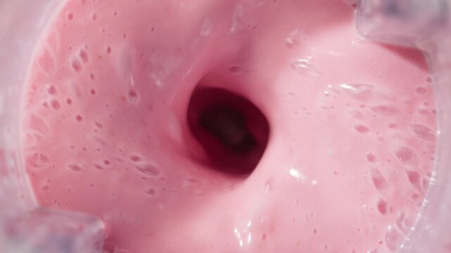 Strawberry and banana pink milkshake blended in blender with splashes. top view. slow motion. Healthy protein smoothie drink concept , food closeup. Protein powder falling in smoothie from spoon