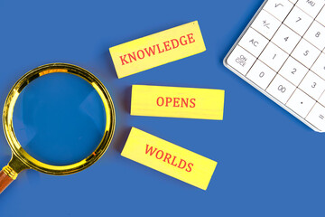 Education,student,university concept. KNOWLEDGE OPENS WORLDS made of wooden blocks on blue background next to calculator, top view