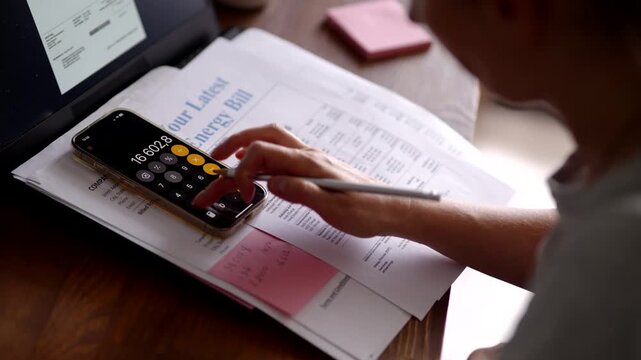 Person using smartphone calculator and pen to pay bills and manage finances