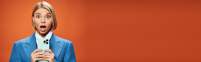 Blonde woman poses stylishly in trendy outfit against an orange backdrop