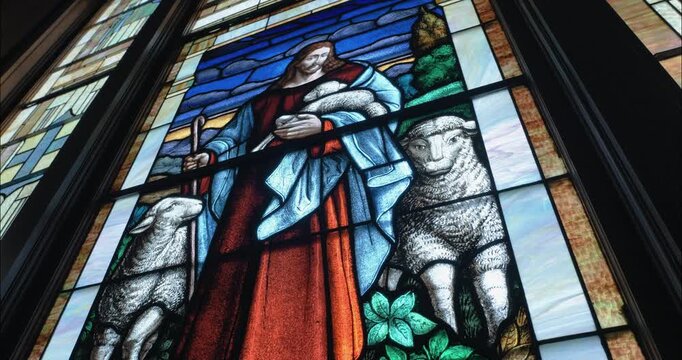 Religious stained-glass window with Jesus and sheep illuminates a church sanctuary, highlighting artistry, devotion, and sacred storytelling.
