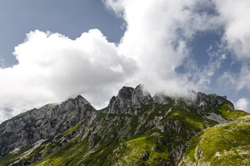 Naklejka premium isolated mountain peaks under bright blue sky with white fluffy clouds. rugged mountain range covered by greenery. artistic background with