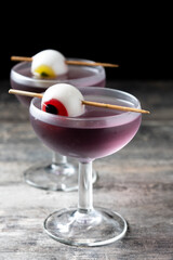Purple Halloween cocktail garnished with candy eye on wooden table