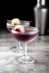 Purple Halloween cocktail garnished with candy eye on wooden table