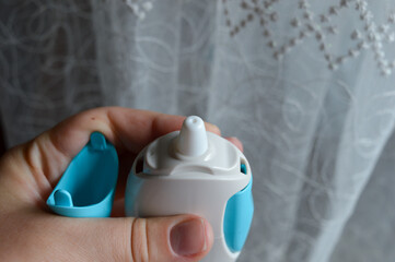 Close-up of a hand holding a nasal spray bottle with blue button, used for allergy, cold, or sinus...