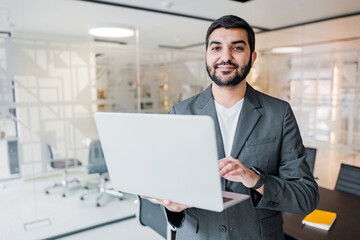 Fototapeta premium Professional man in smart suit confidently presenting laptop in modern office environment