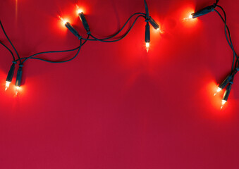Christmas garland lights on red paper  background.  Flat lay.