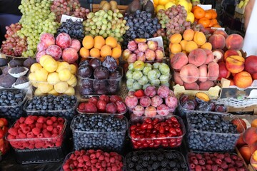 Colorful assortment of fresh fruits and berries at the market — grapes, plums, peaches, raspberries, blackberries, blueberries, apricots, and other seasonal produce