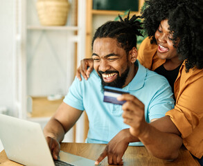 portrait of happy smiling young couple using a laptop computer and a credit card  for online shopping at home, technology and internet use in everyday life concept