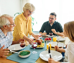 Happy multi-generation family gathering around dining table and having fun during a lunch or dinner on holiday or weekend, senior couple, grandparents, grandmother and grandfather eating