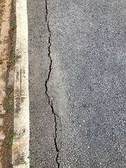 Close-up of a cracked asphalt road beside a concrete curb, illustrating road damage, infrastructure issues, and maintenance needs