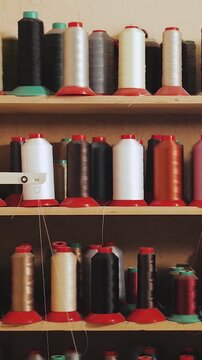 Vertical video. Threads in spools of different colors stand on a wooden shelf in a shoemaker's workshop. A store selling threads and textiles. Slow motion.