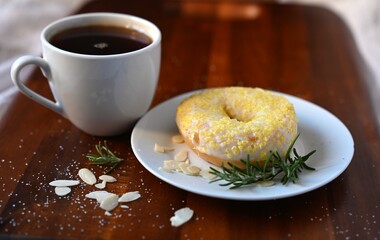 A warm and inviting scene featuring a lemon-glazed donut with a sprig of rosemary and a hot cup of coffee. The setting evokes a sense of comfort and a sweet treat for a cold autumn day.