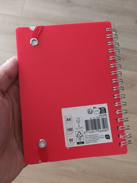 Person holding a red spiral notebook with a barcode on the back