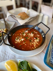 Traditional greek saganaki with feta cheese in tomato sauce, a hot appetizer served in a pan at a restaurant table for lunch, concept of authentic mediterranean cuisine, food travel, taverna menu