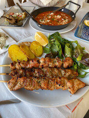 Grilled chicken souvlaki skewers on a plate with potatoes and fresh salad, a traditional dish served for lunch in a greek taverna, concept of mediterranean cuisine, food travel, restaurant menu