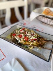 Baked greek eggplant with feta cheese and tomatoes, a healthy vegetarian appetizer served on a plate in a traditional taverna, concept of mediterranean diet, healthy restaurant menu, food blog