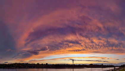Clouds burn in a fiery sunset. Hot streams of multi-level meteorological layers. Cumulus and cirrus clouds form a grand epic picture of a play of colors. Orange gradient with edge of city buildings.