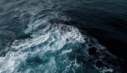 Fototapeta premium Bright sunlight reflects on the tranquil ocean as waves gently lap at the surface, creating a stunning interplay of blues and whites near the shoreline. The calmness of the scene evokes peace